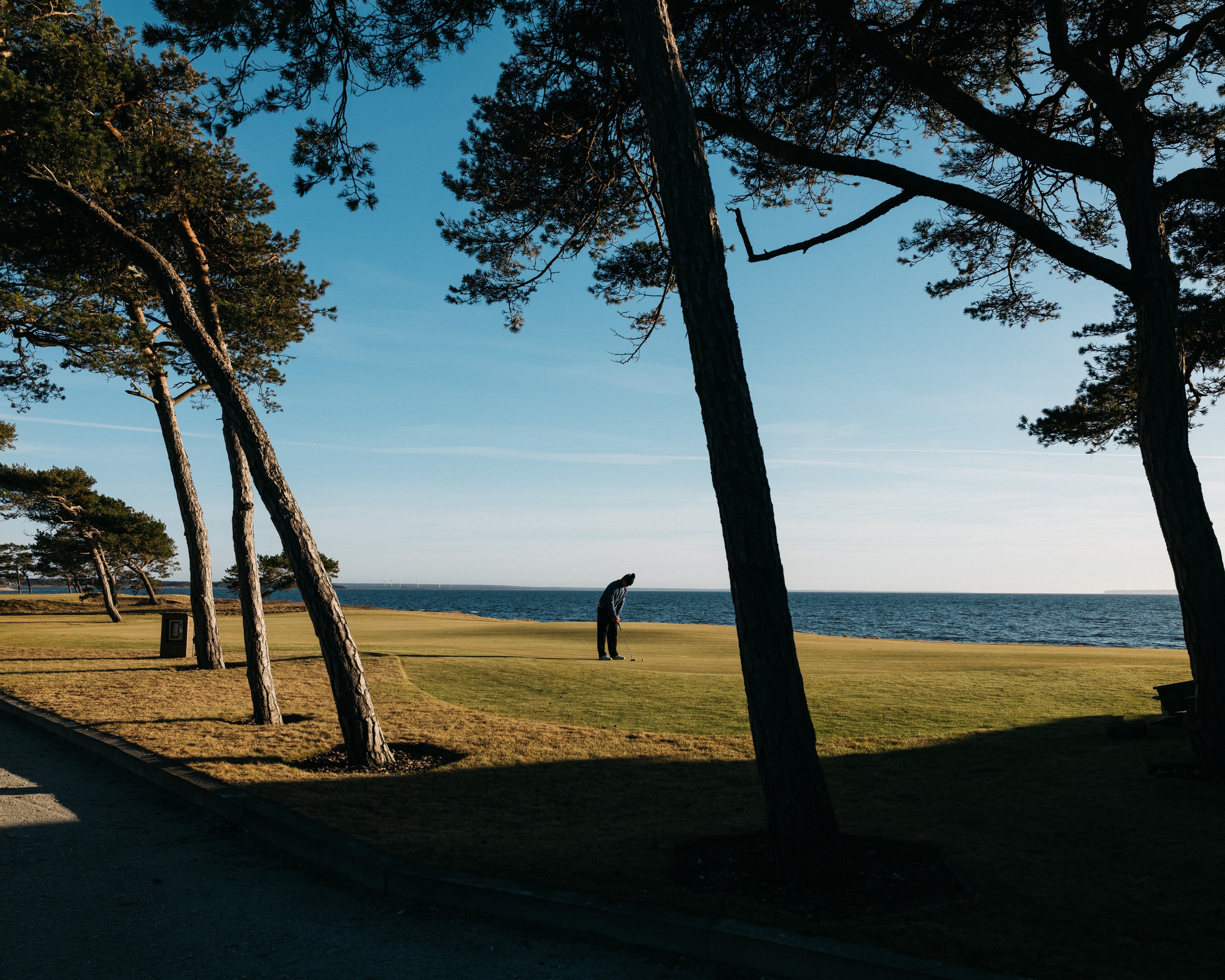 Golfspelare på grön fairway vid golfbana nära Uppsala med klubba i handen och stadens silhuett i bakgrunden